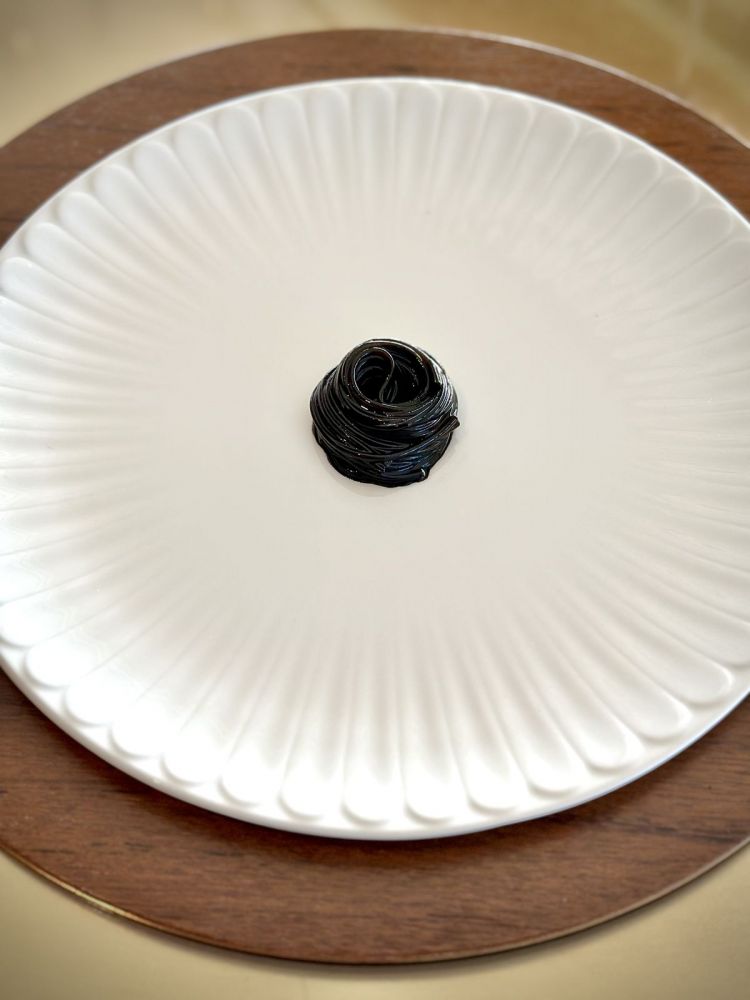 Rotella di pasta alla liquirizia: un predessert inconsueto. Si tratta di spaghettini cotti un po’ di più e finiti in uno sciroppo di zucchero con nero di seppia e liquirizia. Quando si raffreddano, la pasta assume la stessa texture della rotella Haribo. Sperimentazione, avanguardia e divertimento