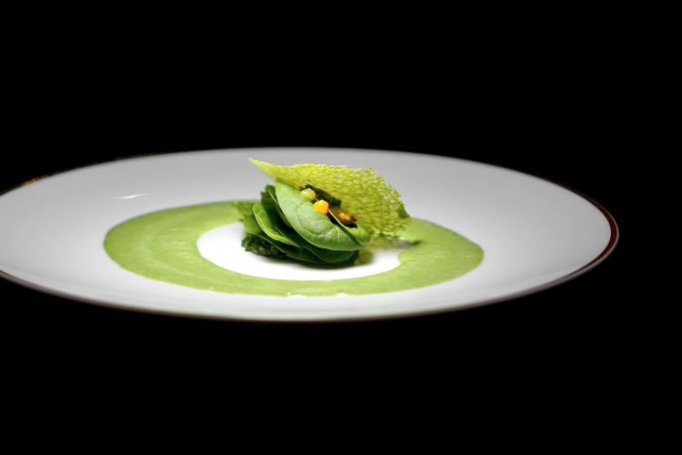 Torta di bietole: un velo di sfoglia brisè scottata alla plancia aromatizzata alla crema di spinacio gigante. Battuto di alghe come un pesto marino, sfoglie di spinacio novello insaporite da una pomata di limone e arancia al frutto della passione. Polvere di Grana Padano 24 mesi e fonduta allo spinacio
